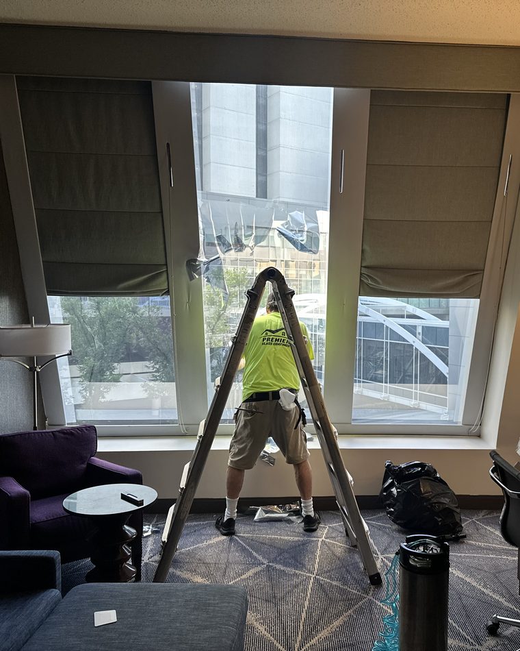 A Premier Glass Coatings installer on a stepladder applying film to a hotel room window in Atlanta