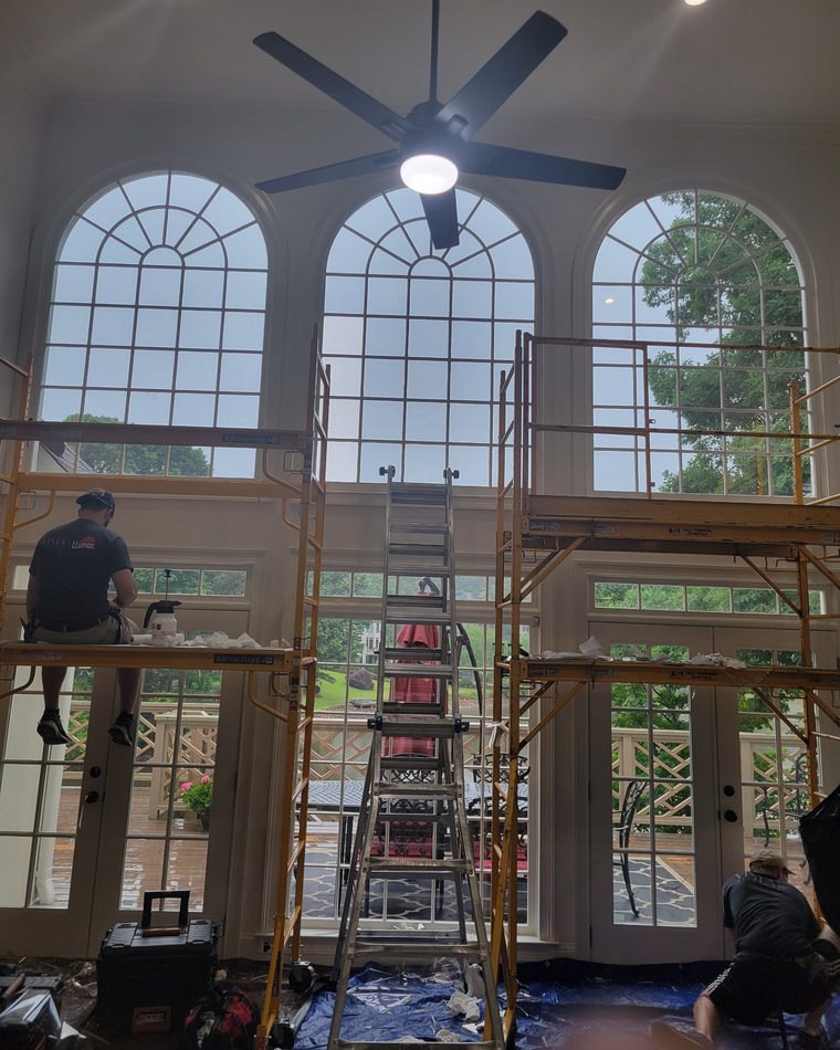 Installers on scaffolding applying window film to two-story arched windows and French doors in a home's great room